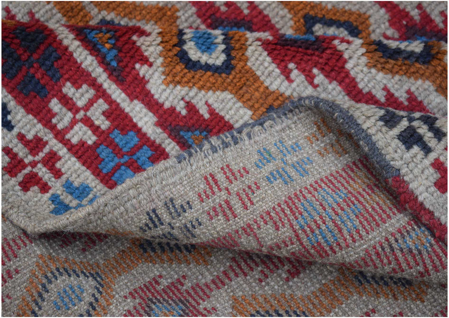 A handmade Afghan Pashm rug featuring a geometric tribal pattern in red, blue, and ivory wool.