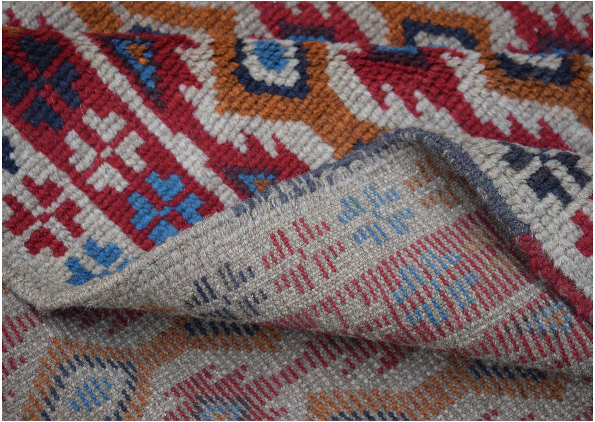 A handmade Afghan Pashm rug featuring a geometric tribal pattern in red, blue, and ivory wool.