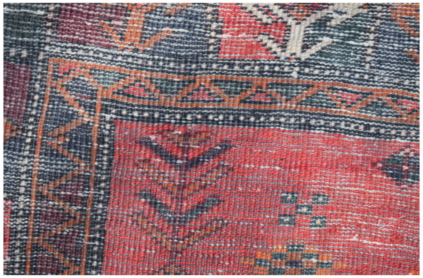 A close-up of a vintage Afghan Baluch wool rug featuring geometric patterns in red and blue tones.