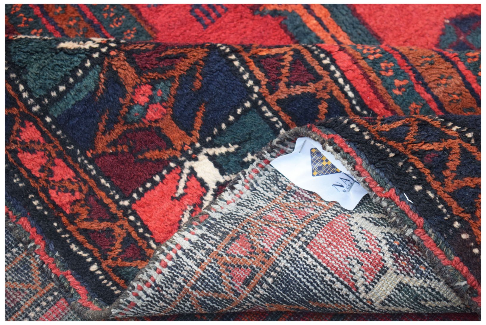 A folded vintage Afghan Baluch wool rug featuring a geometric pattern in red, blue, and green.