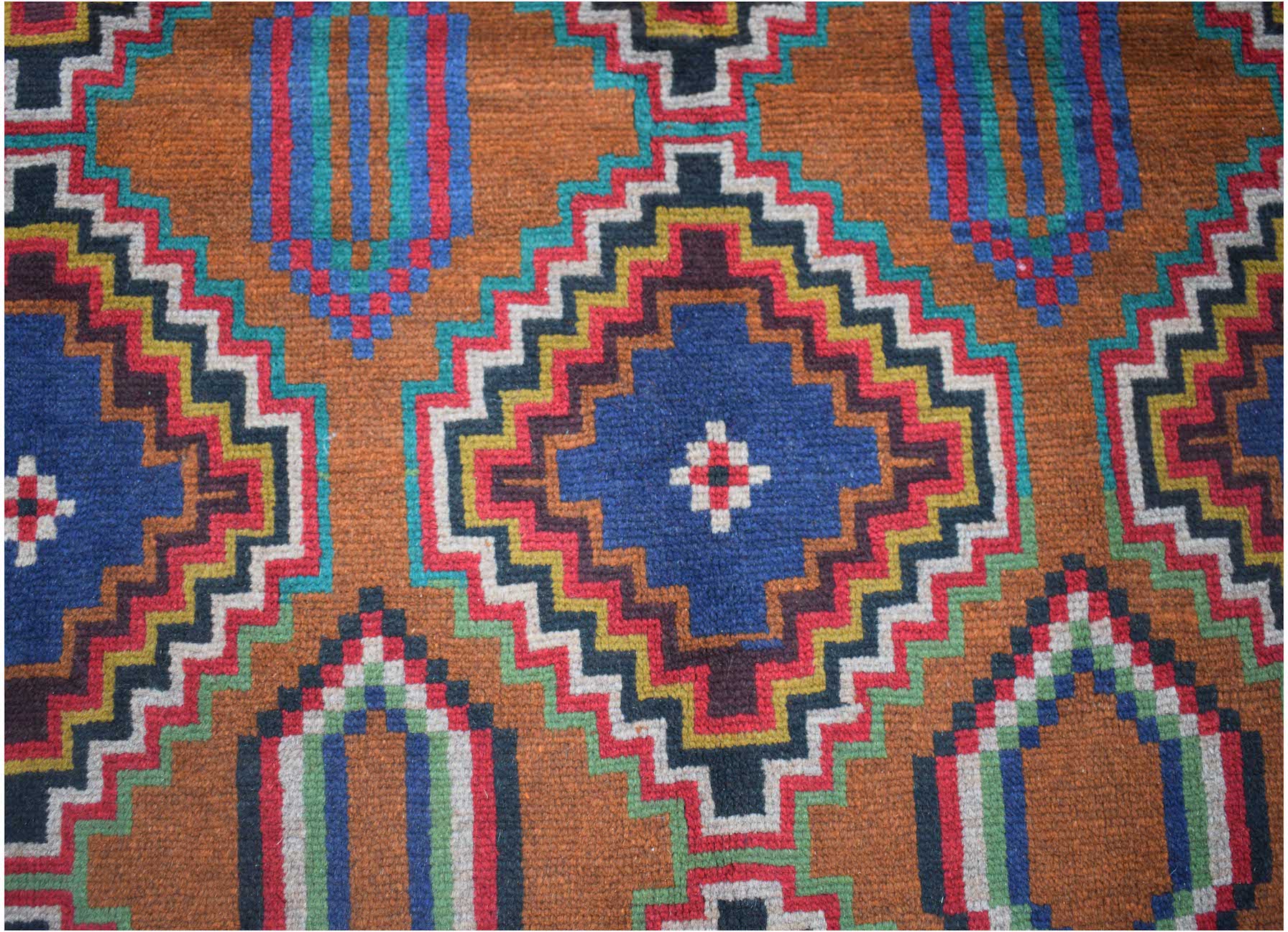 Handmade Afghan Pashm rug featuring a geometric diamond pattern in blue, red, and earthy tones.
