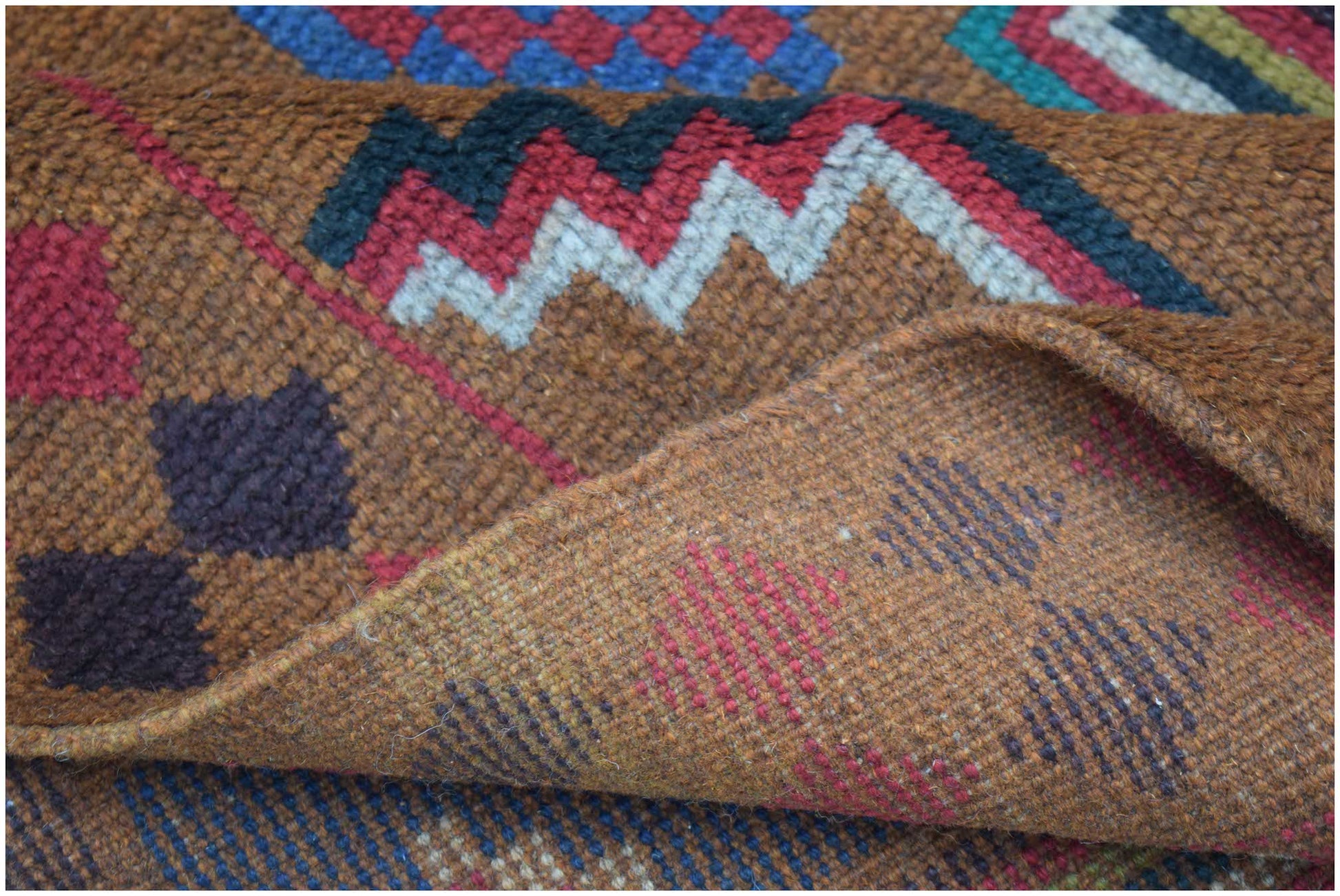 A handmade Afghan Pashm rug featuring geometric patterns in shades of brown, red, and blue.