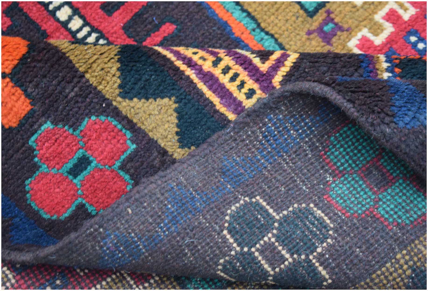 A handmade Afghan Pashm rug featuring a dark, geometric tribal pattern in red, blue, and brown.