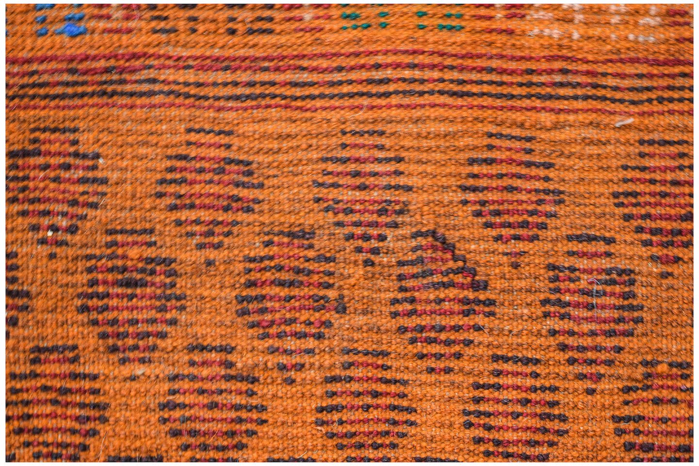A handmade Afghan Pashm rug featuring a geometric pattern in shades of orange, brown, and red.