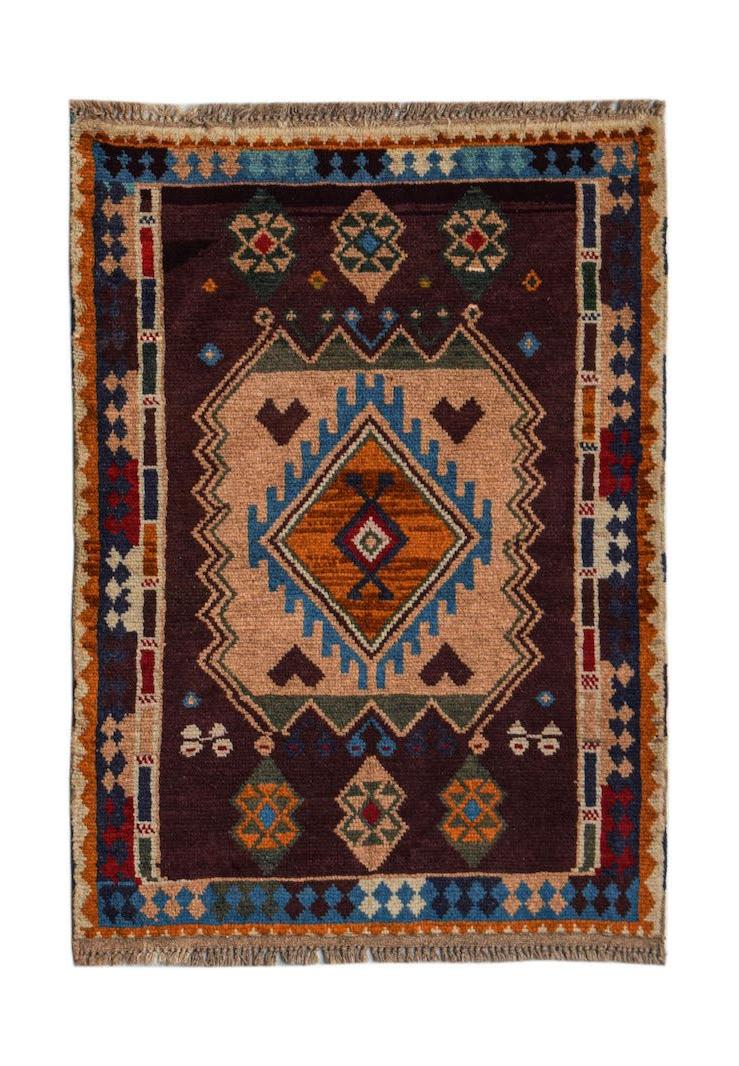A handmade Afghan Pashm rug featuring a central diamond motif in earthy tones on a dark background.