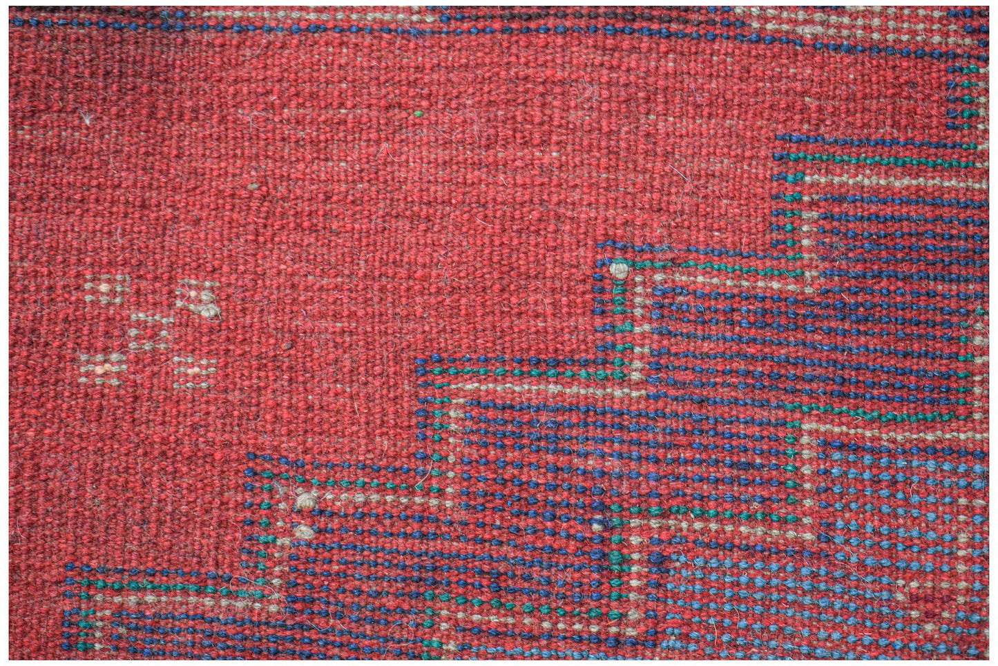 A handmade Afghan Pashm rug featuring a geometric pattern in deep red, blue, and ivory wool.