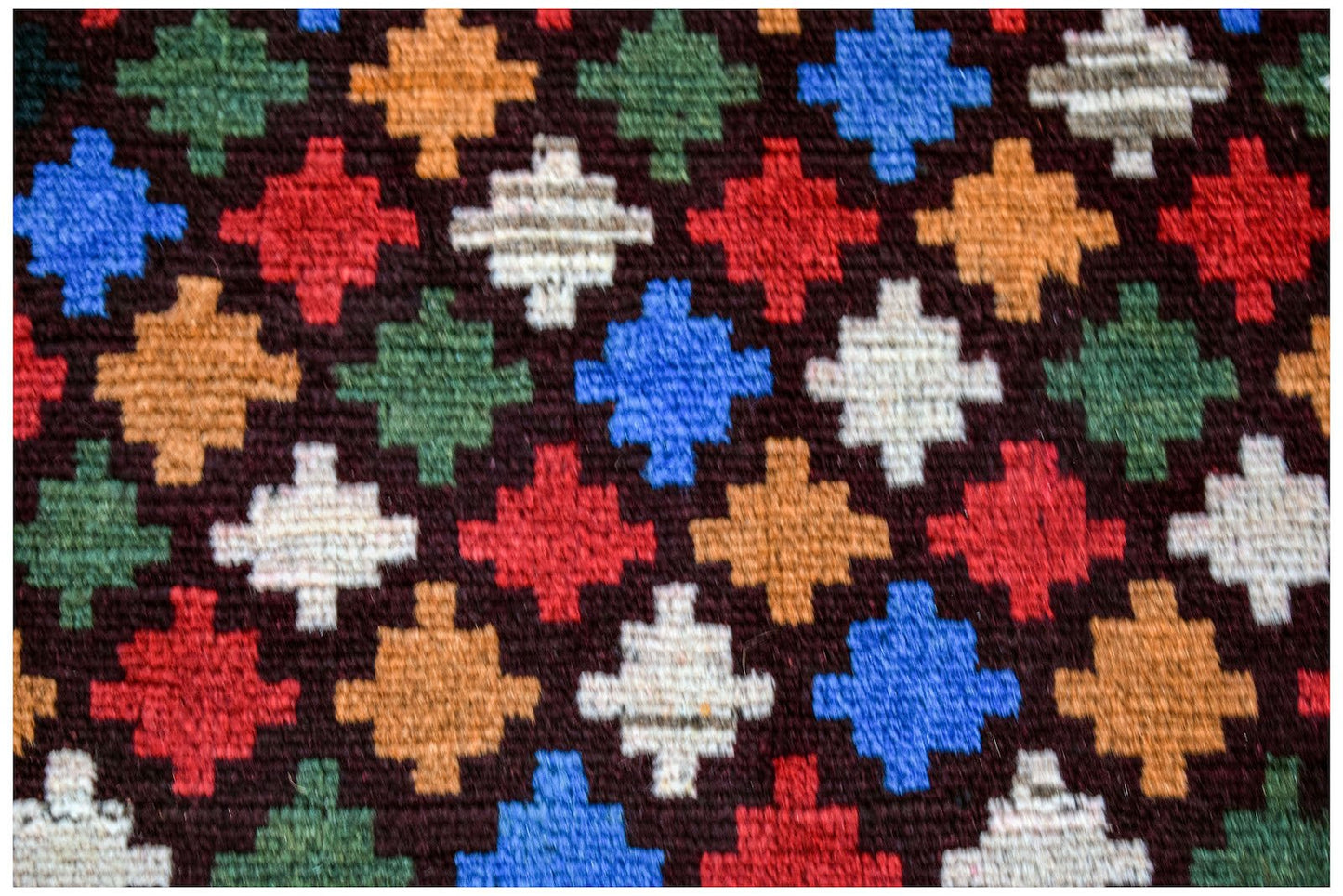 Handmade Afghan wool rug featuring a repeating geometric pattern in red, blue, green, and ivory.