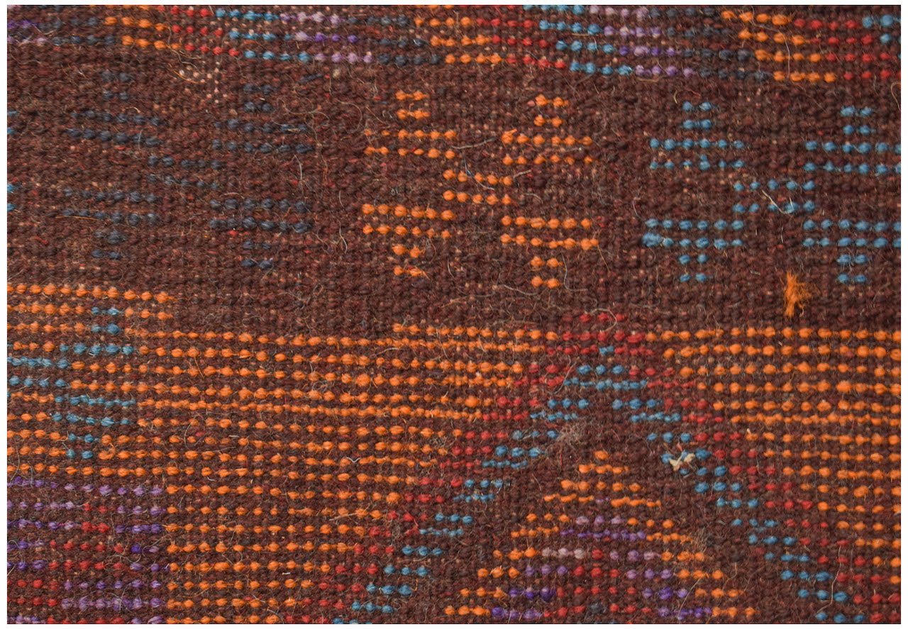 A close-up of a handmade Afghan wool rug featuring geometric patterns in orange, blue, and purple.