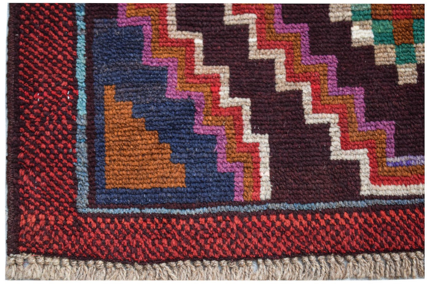 A handmade Afghan Pashm rug featuring a geometric zigzag pattern in red, blue, and brown wool.
