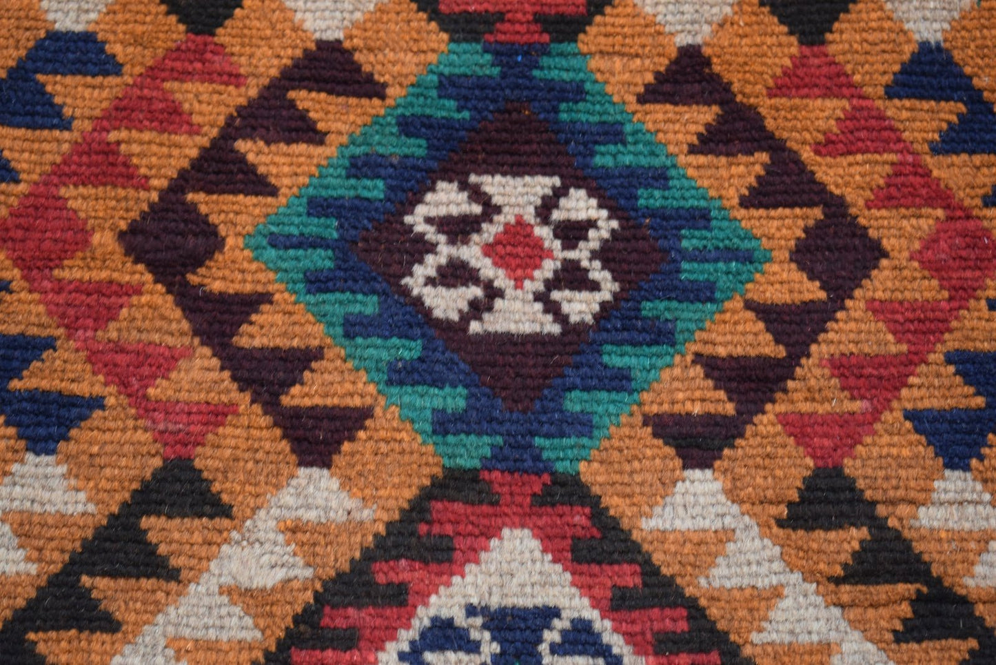 A handmade Afghan Pashm rug featuring a geometric diamond pattern in red, blue, brown, and ivory.