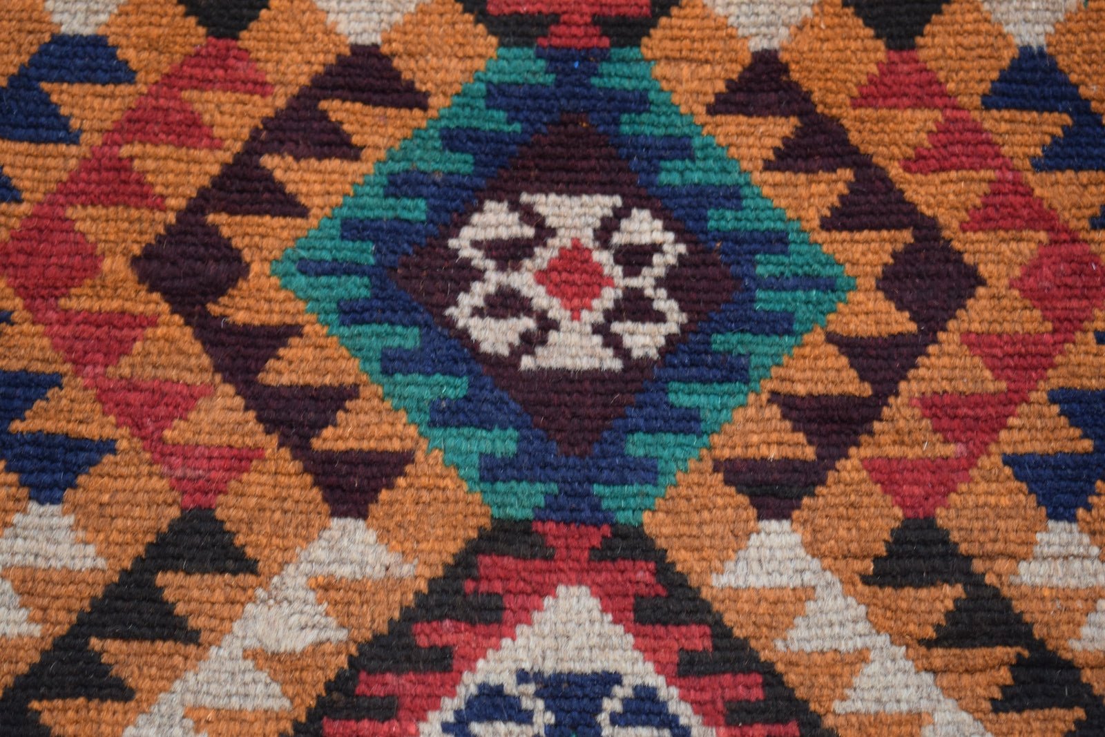 A handmade Afghan Pashm rug featuring a geometric diamond pattern in red, blue, brown, and ivory.