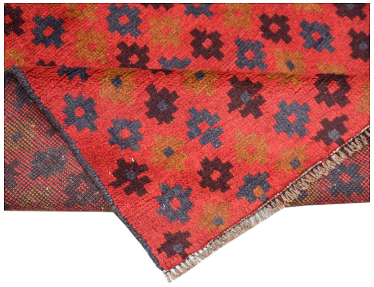 A handmade Afghan Pashm rug featuring a repeating geometric floral pattern in red, brown, and blue.