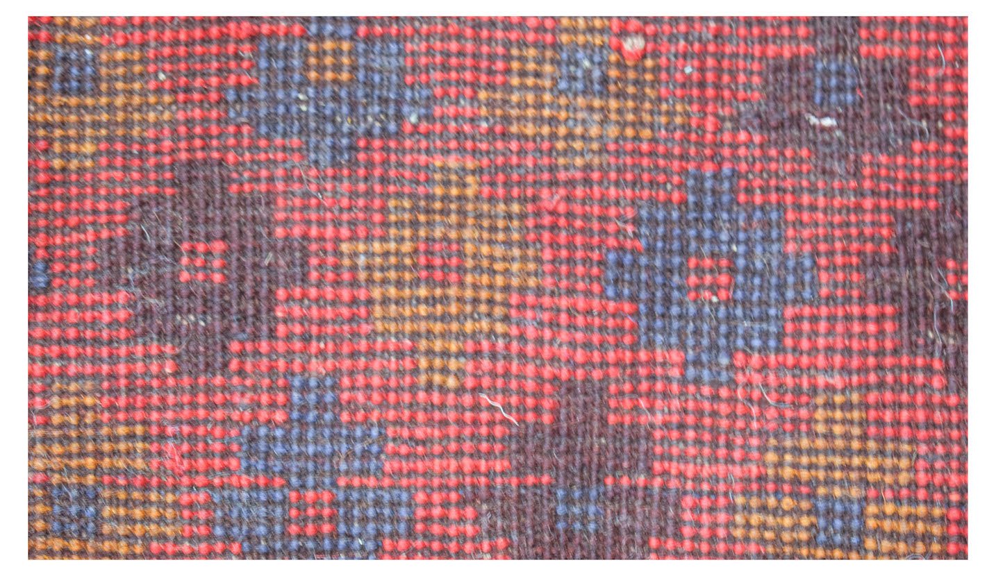 A close-up of a handmade Afghan Pashm rug featuring a geometric pattern in red, blue, and brown.