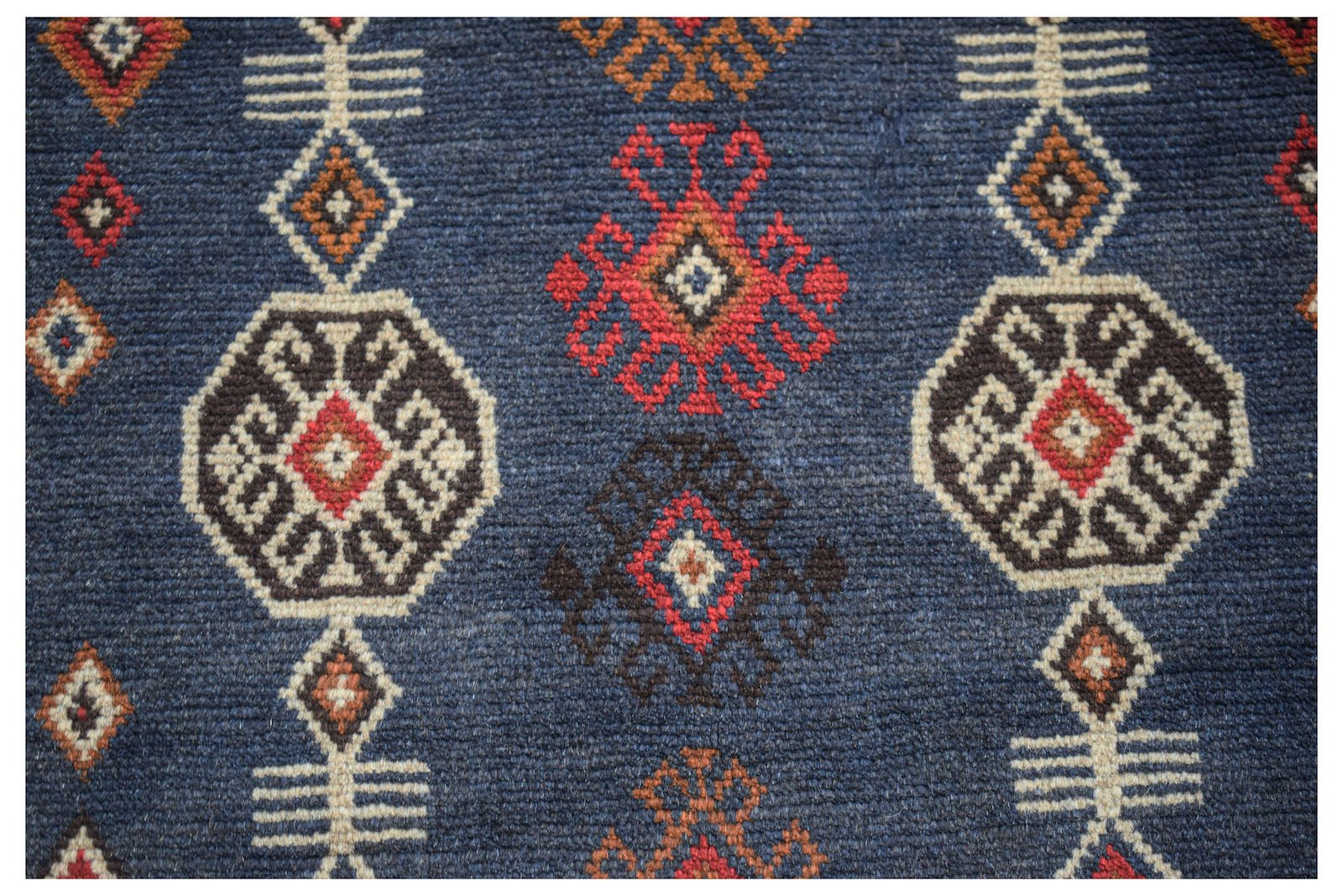 Handmade Afghan Pashm rug featuring a dark blue field with geometric tribal patterns in red and tan.