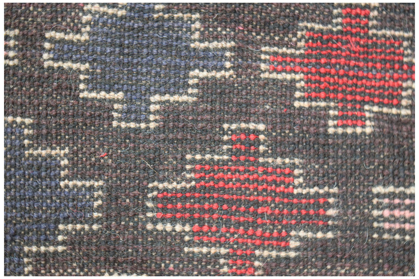 A close-up of a handmade Afghan wool rug featuring geometric patterns in red, blue, and ivory.
