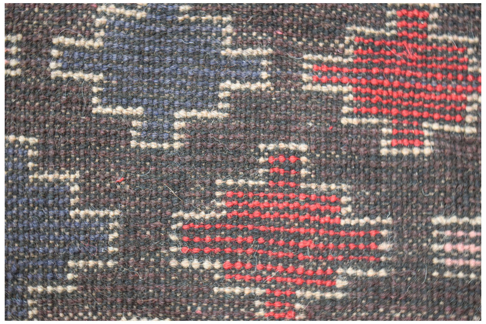 A close-up of a handmade Afghan wool rug featuring geometric patterns in red, blue, and ivory.