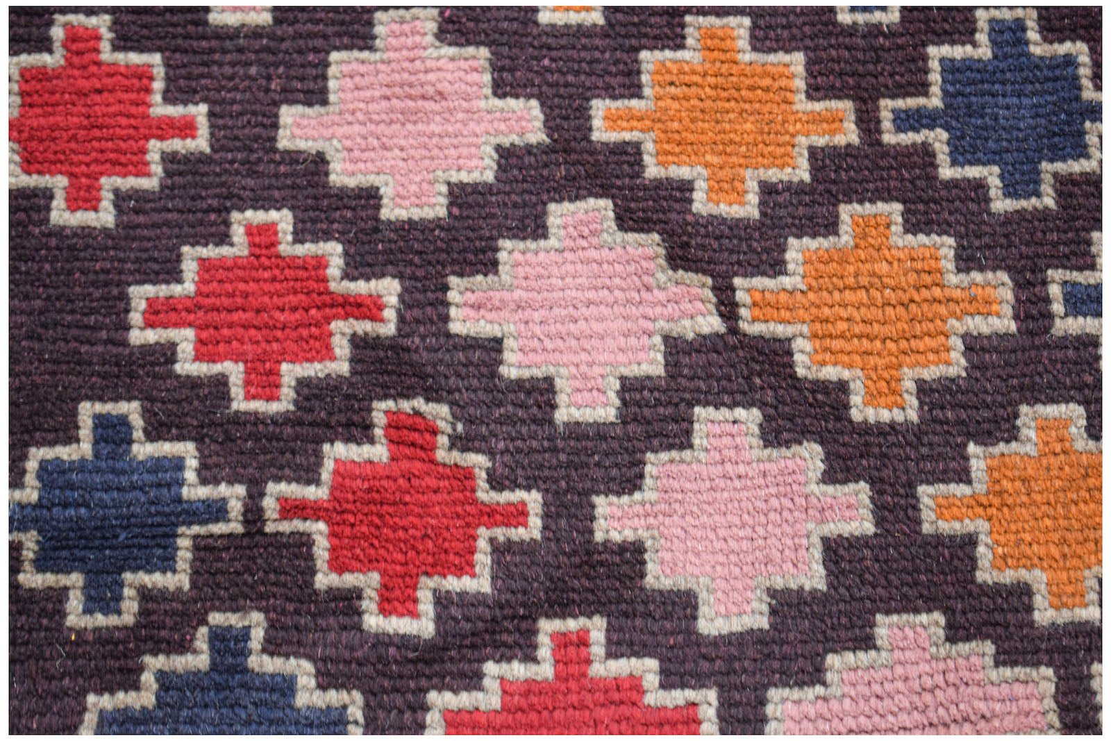 Handmade Afghan Pashm rug featuring a repeating geometric cross pattern in red, pink, and orange.