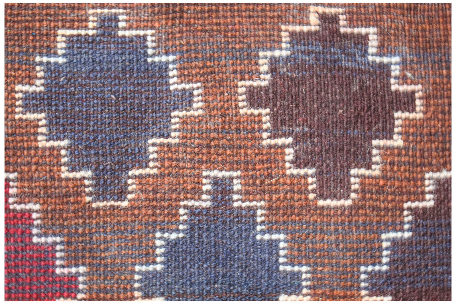 A close-up of a handmade Afghan wool rug featuring geometric patterns in blue, brown, and red.