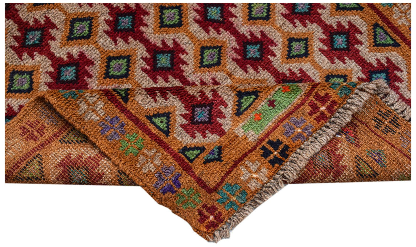 A handmade Afghan Pashm rug featuring a geometric tribal pattern in red, brown, and blue tones.