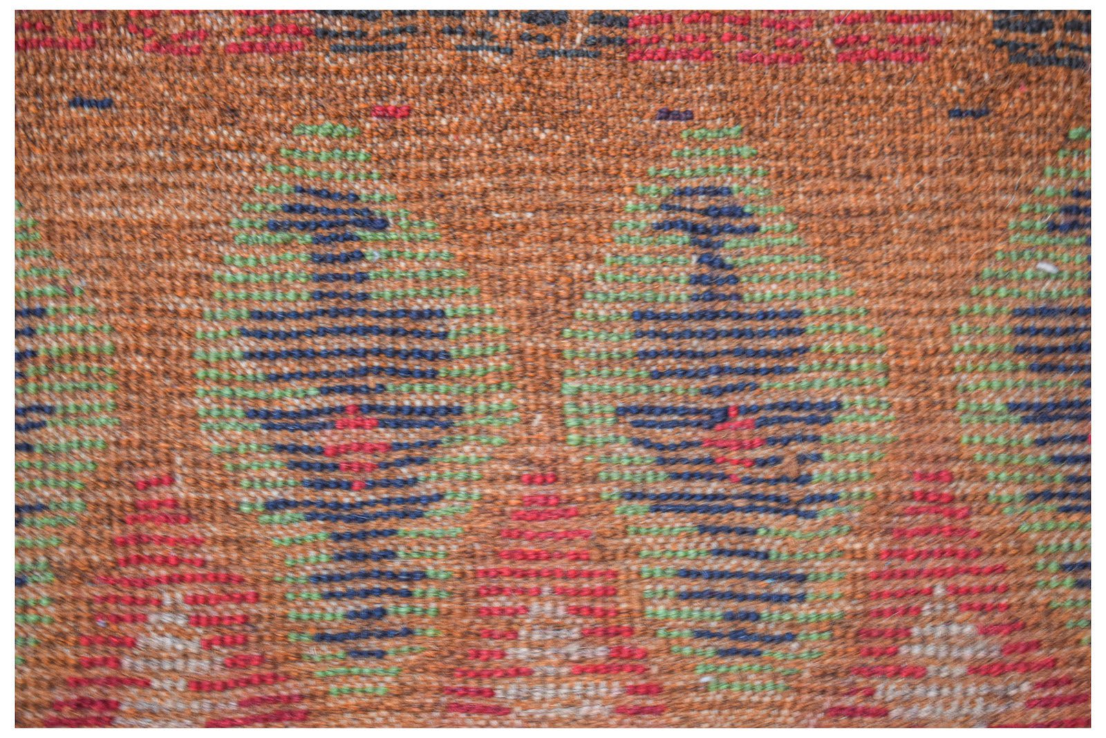 A handmade Afghan Pashm rug featuring a tribal pattern in shades of brown, blue, green, and red.