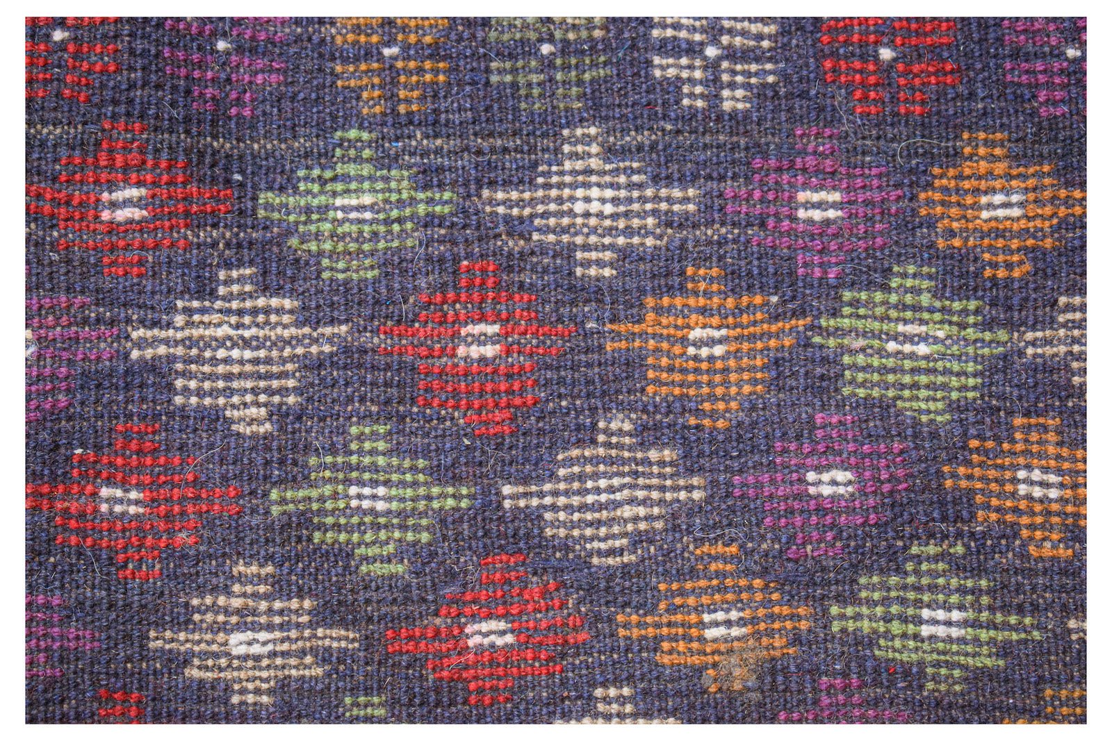 Handmade Afghan Pashm rug featuring a dark blue field with a repeating pattern of colorful motifs.