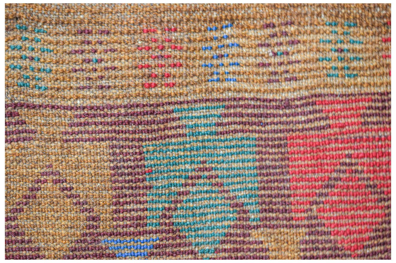 A handmade Afghan Pashm rug featuring a geometric tribal pattern in shades of brown, red, and blue.