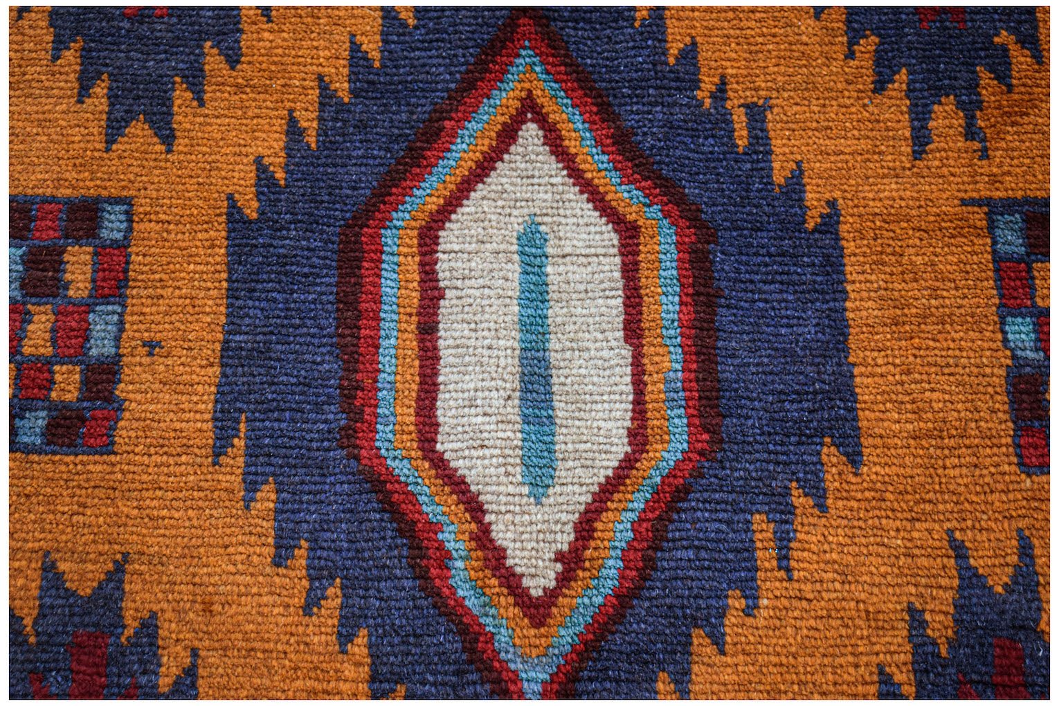Handmade Afghan Pashm rug featuring a central diamond motif in blue, orange, and ivory wool.