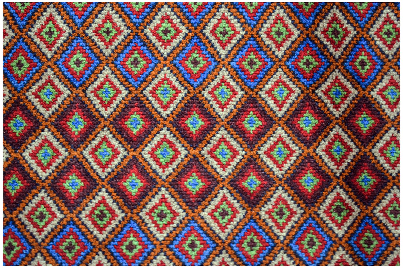 Handmade Afghan Pashm rug featuring a repeating diamond pattern in red, blue, and ivory wool.