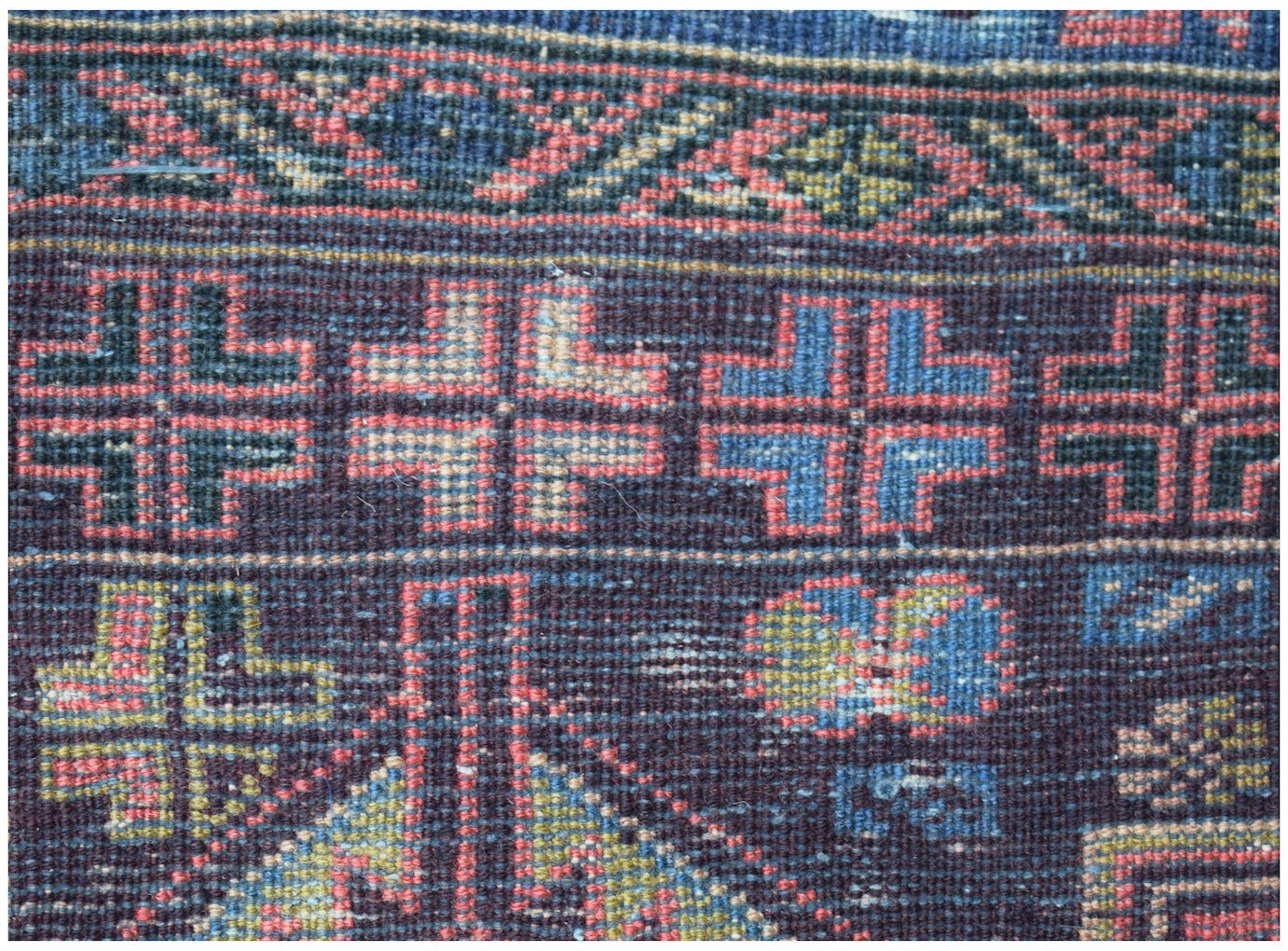 Handmade Afghan Pashm rug featuring geometric cross motifs in blue, red, and ivory on a dark field.