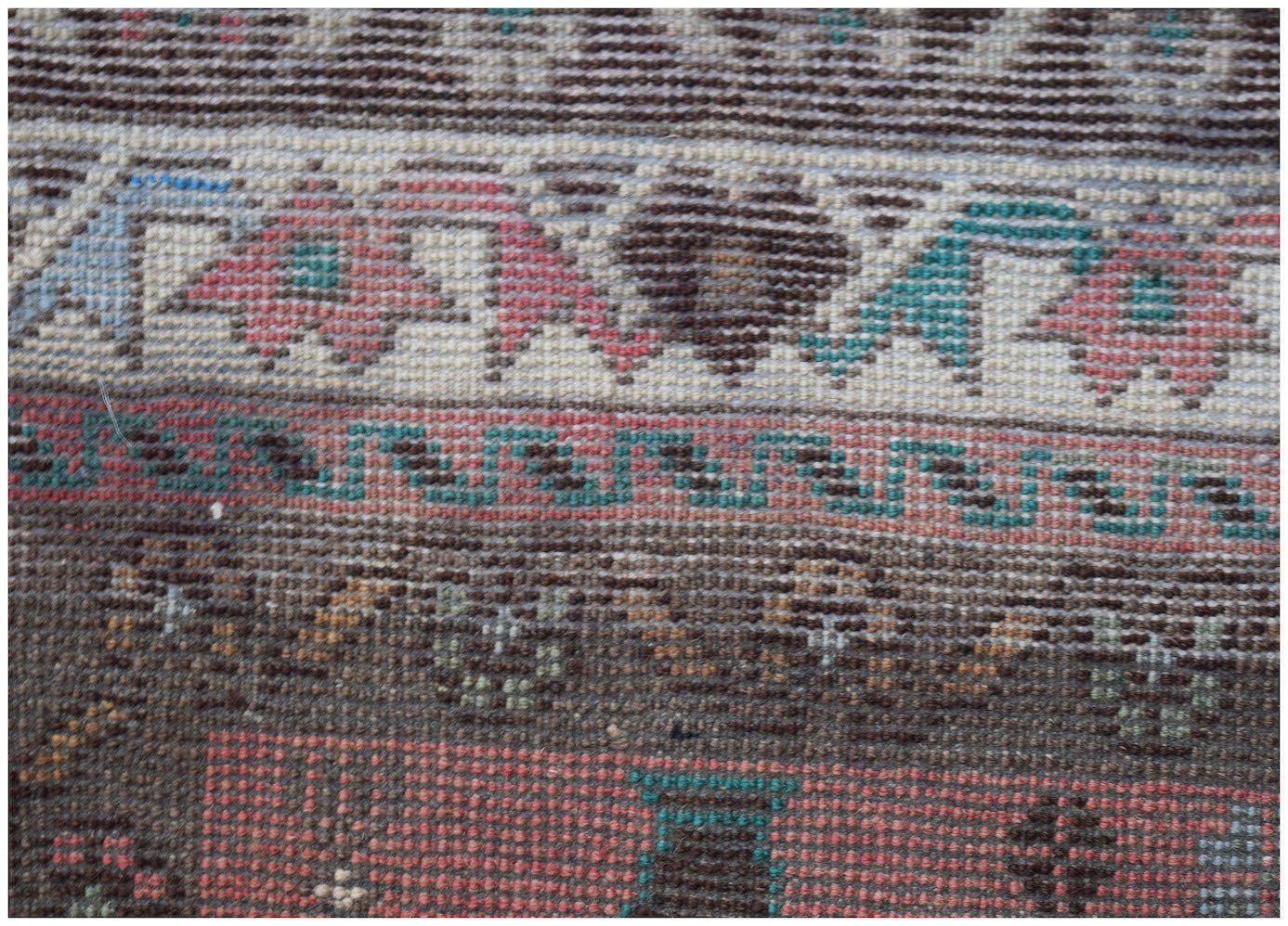A handmade Afghan Pashm rug featuring intricate geometric patterns in red, brown, and blue tones.