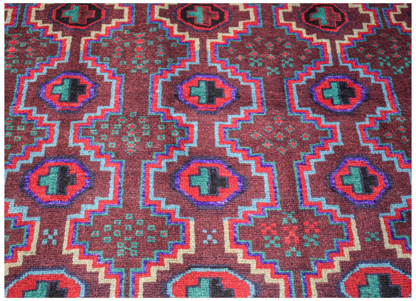 Handmade Afghan Pashm rug featuring a geometric pattern in dark red, blue, and green wool.