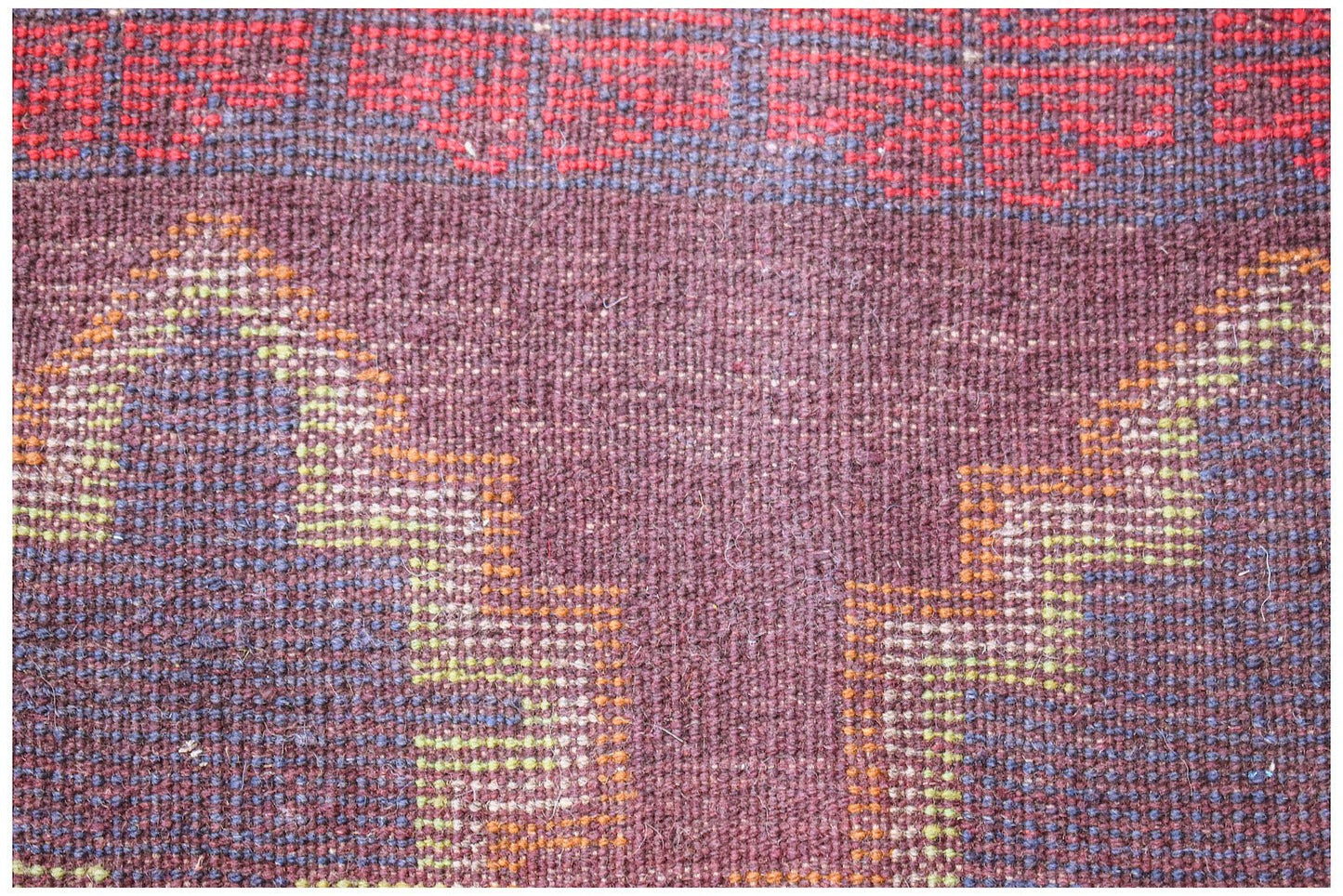 A close-up of a handmade Afghan Pashm rug featuring geometric patterns in red, brown, and blue.