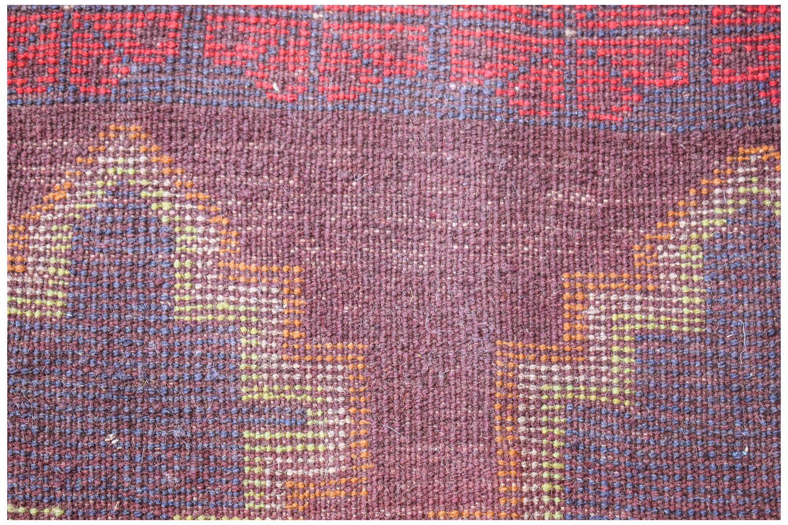 A close-up of a handmade Afghan Pashm rug featuring geometric patterns in red, brown, and blue.