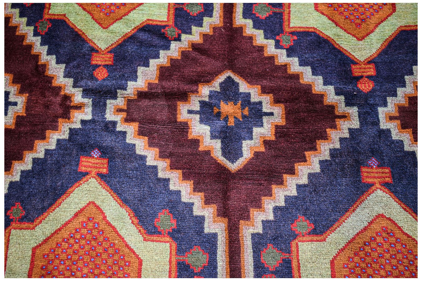 Handmade Afghan Pashm rug featuring a geometric diamond pattern in deep red, blue, and tan wool.