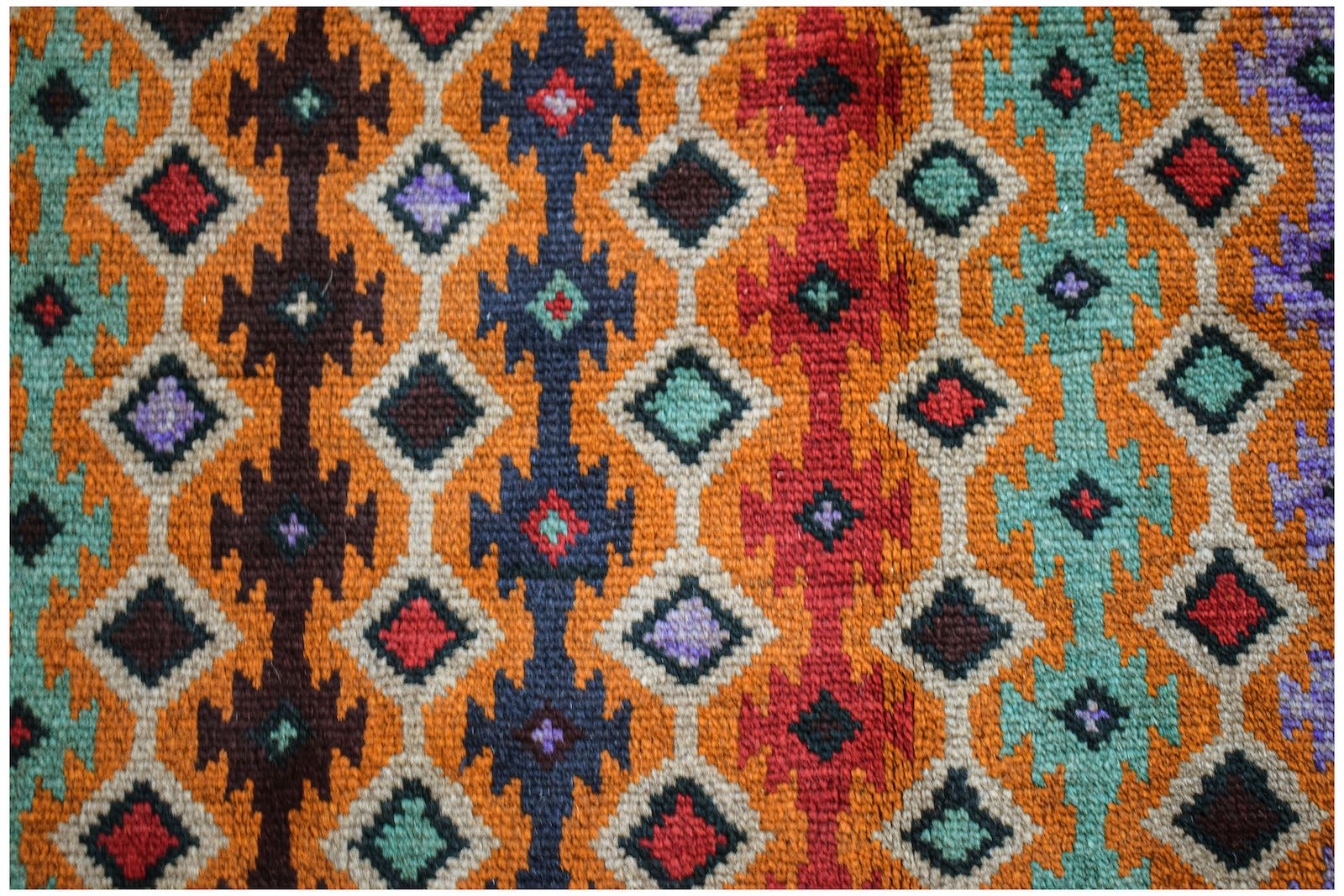 Handmade Afghan Pashm rug featuring a geometric diamond pattern in vibrant red, blue, and orange.
