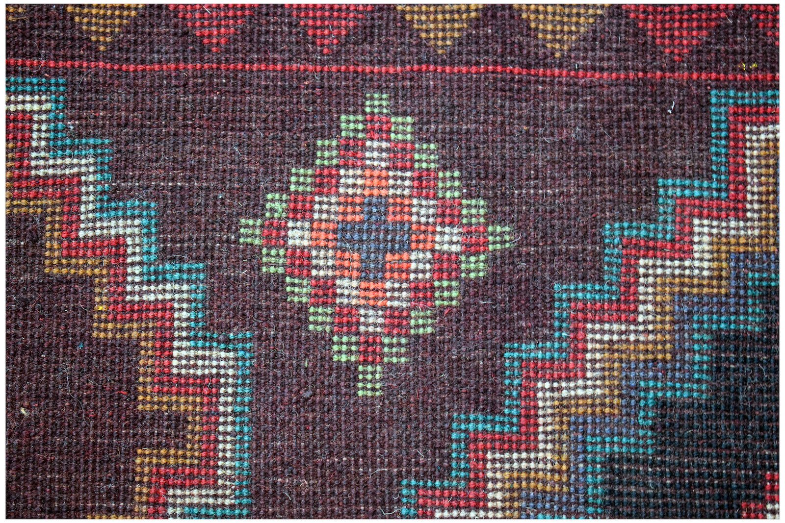 A handmade Afghan Pashm rug featuring a dark brown field with geometric diamond and zigzag patterns.