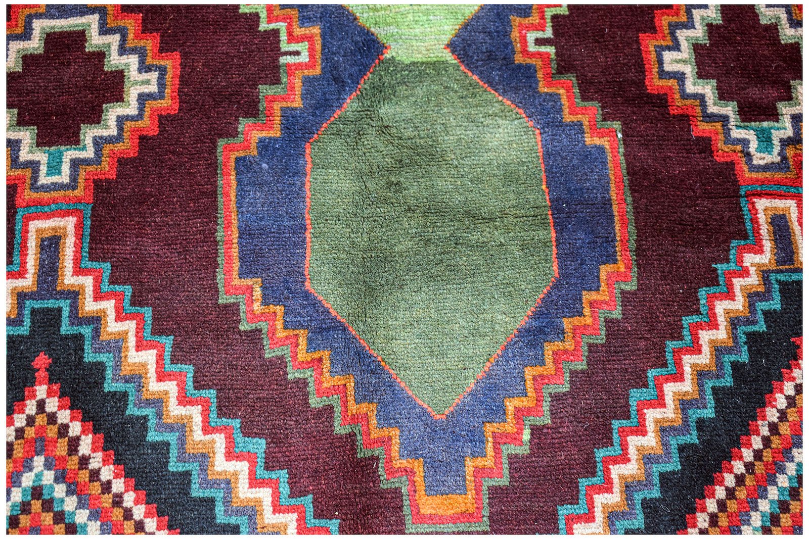 Handmade Afghan Pashm rug featuring a geometric tribal pattern in deep red, blue, and green tones.