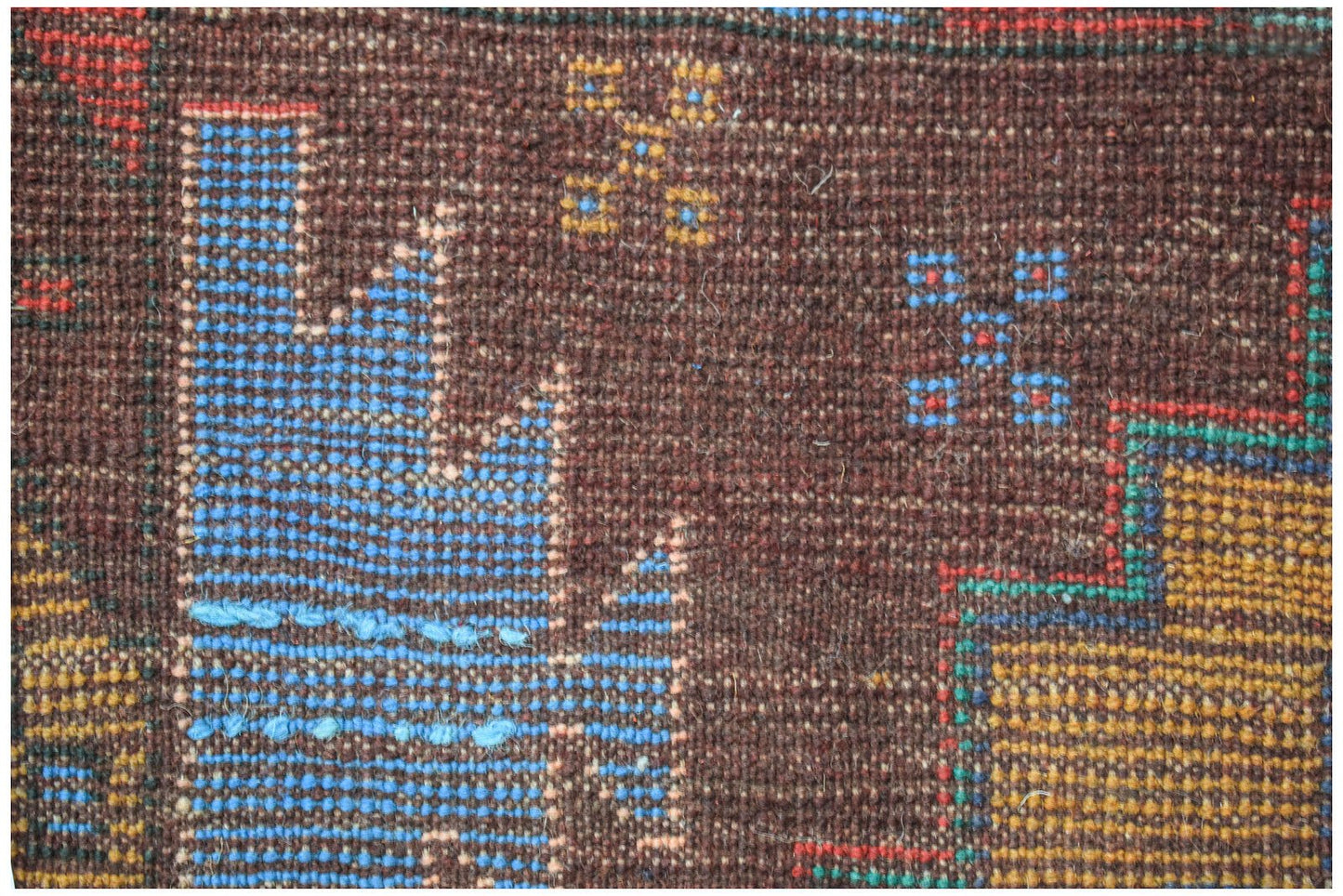 A close-up of a handmade Afghan Pashm rug featuring geometric blue and yellow patterns on brown wool.