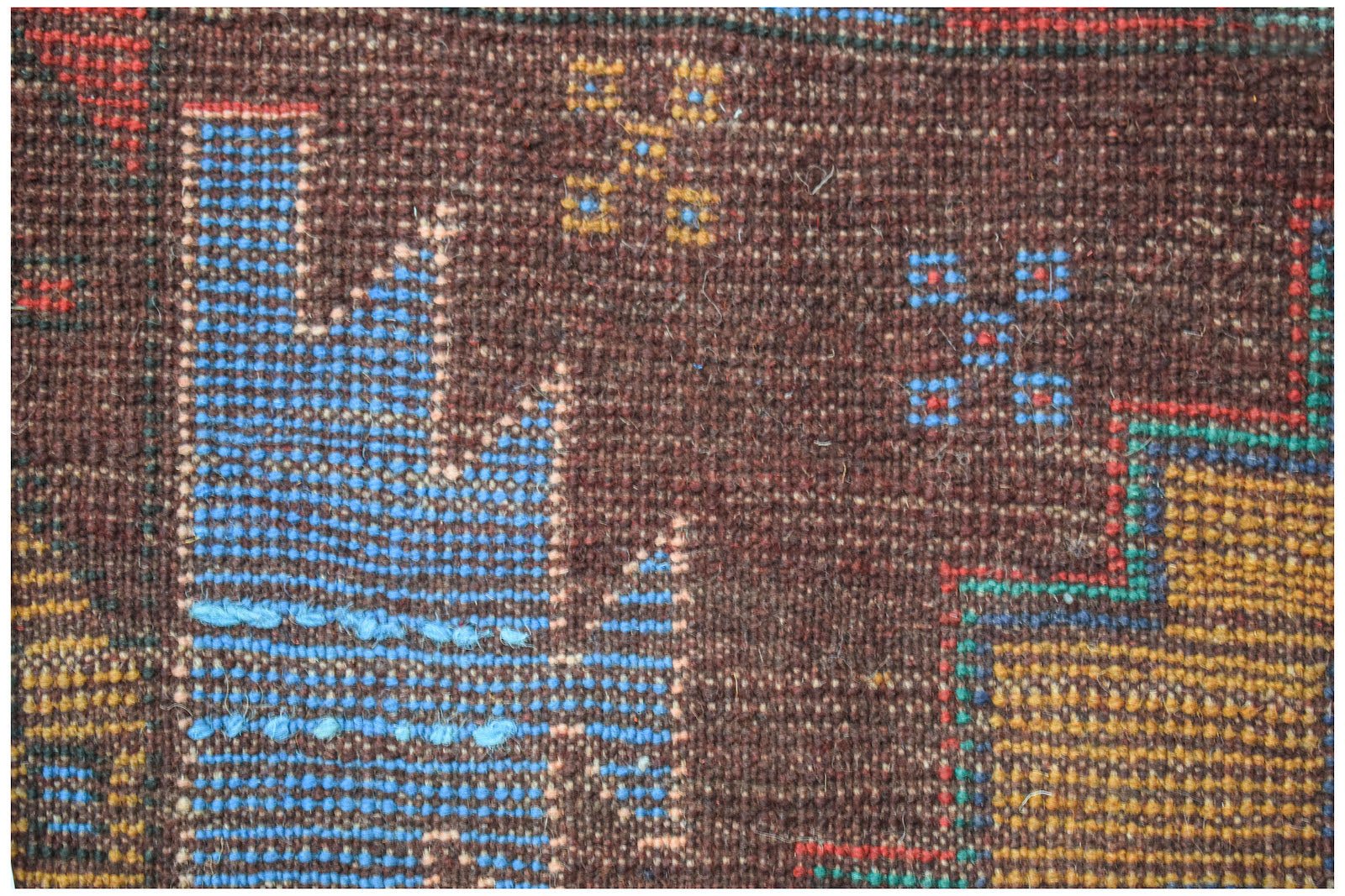 A close-up of a handmade Afghan Pashm rug featuring geometric blue and yellow patterns on brown wool.