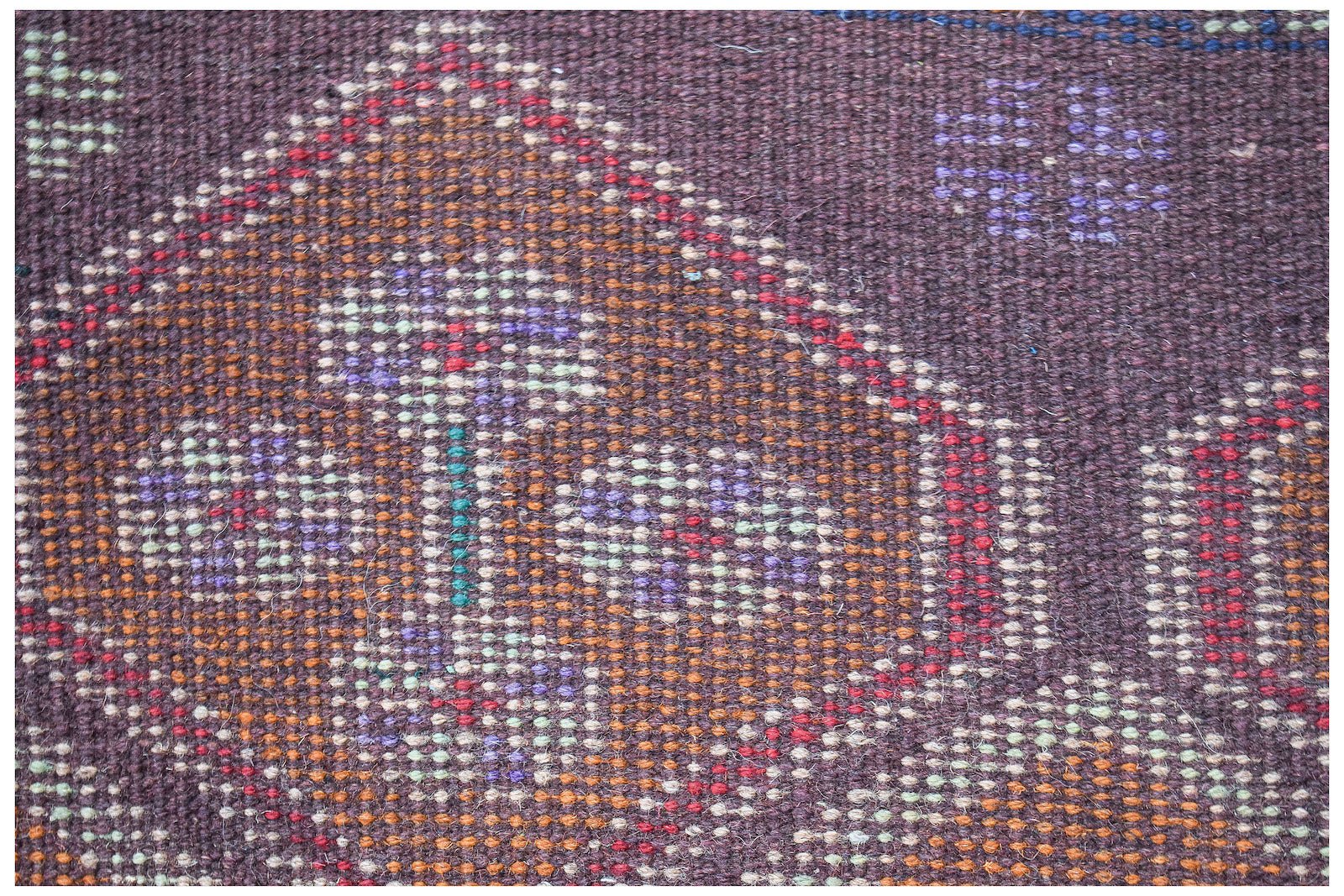 A close-up of a handmade Afghan Pashm rug featuring intricate geometric patterns in dark wool.