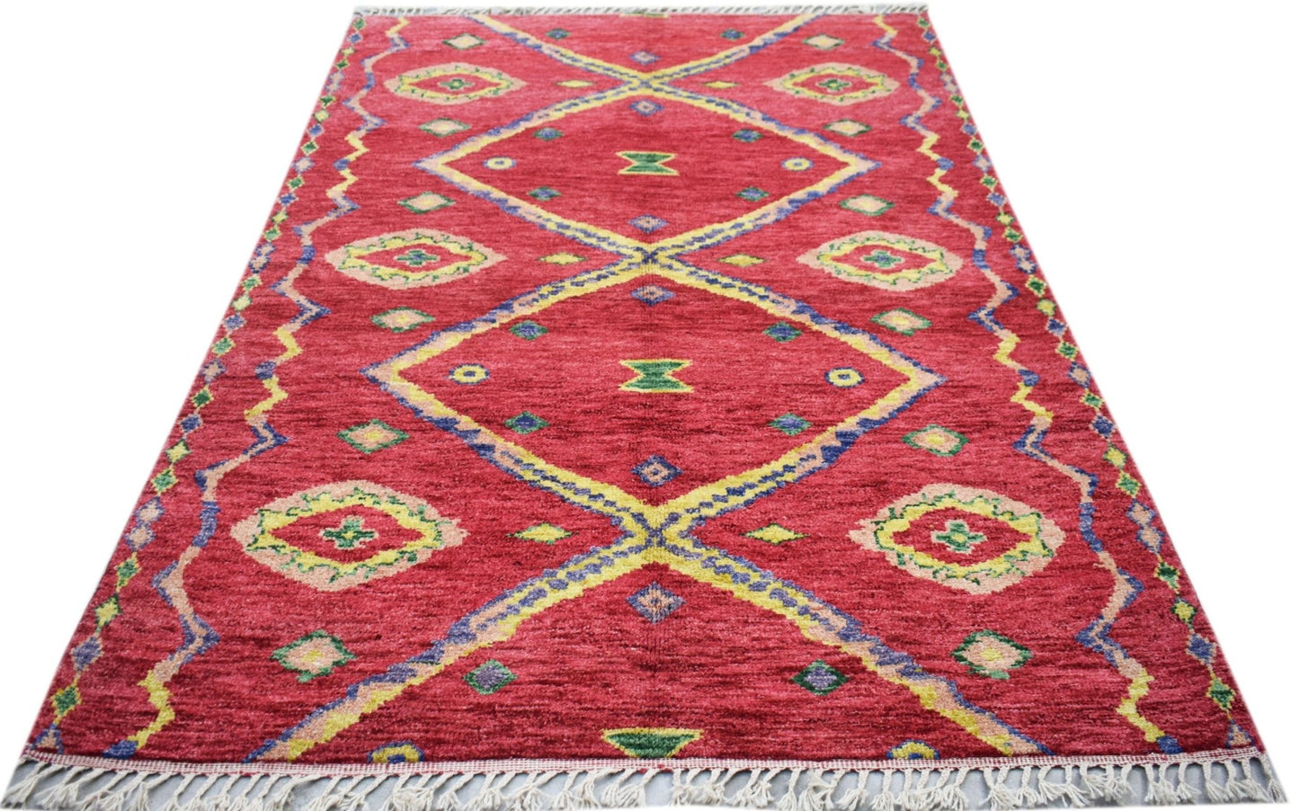 A hand-knotted Afghan wool rug featuring a red field with yellow and blue geometric diamond patterns.