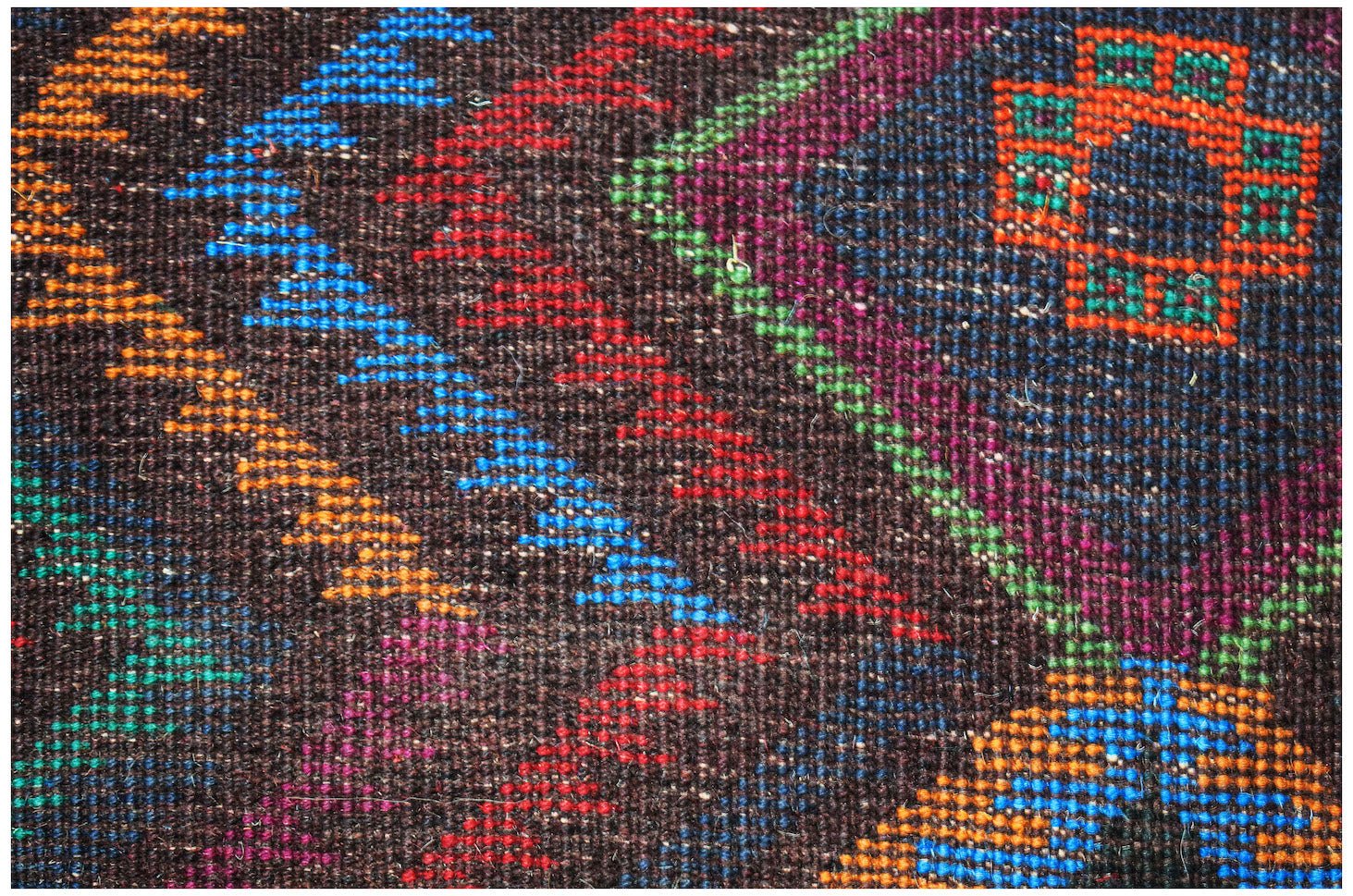 A close-up of a handmade Afghan Pashm rug featuring geometric patterns in vibrant, colorful wool.