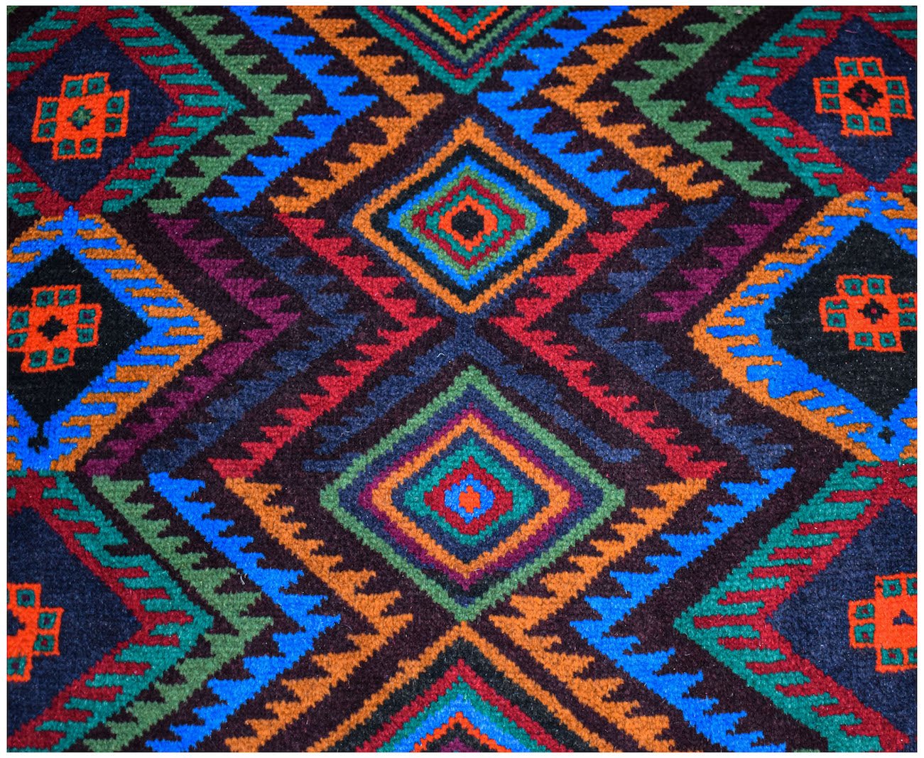Handmade Afghan Pashm rug featuring a geometric diamond pattern in vibrant red, blue, and green.