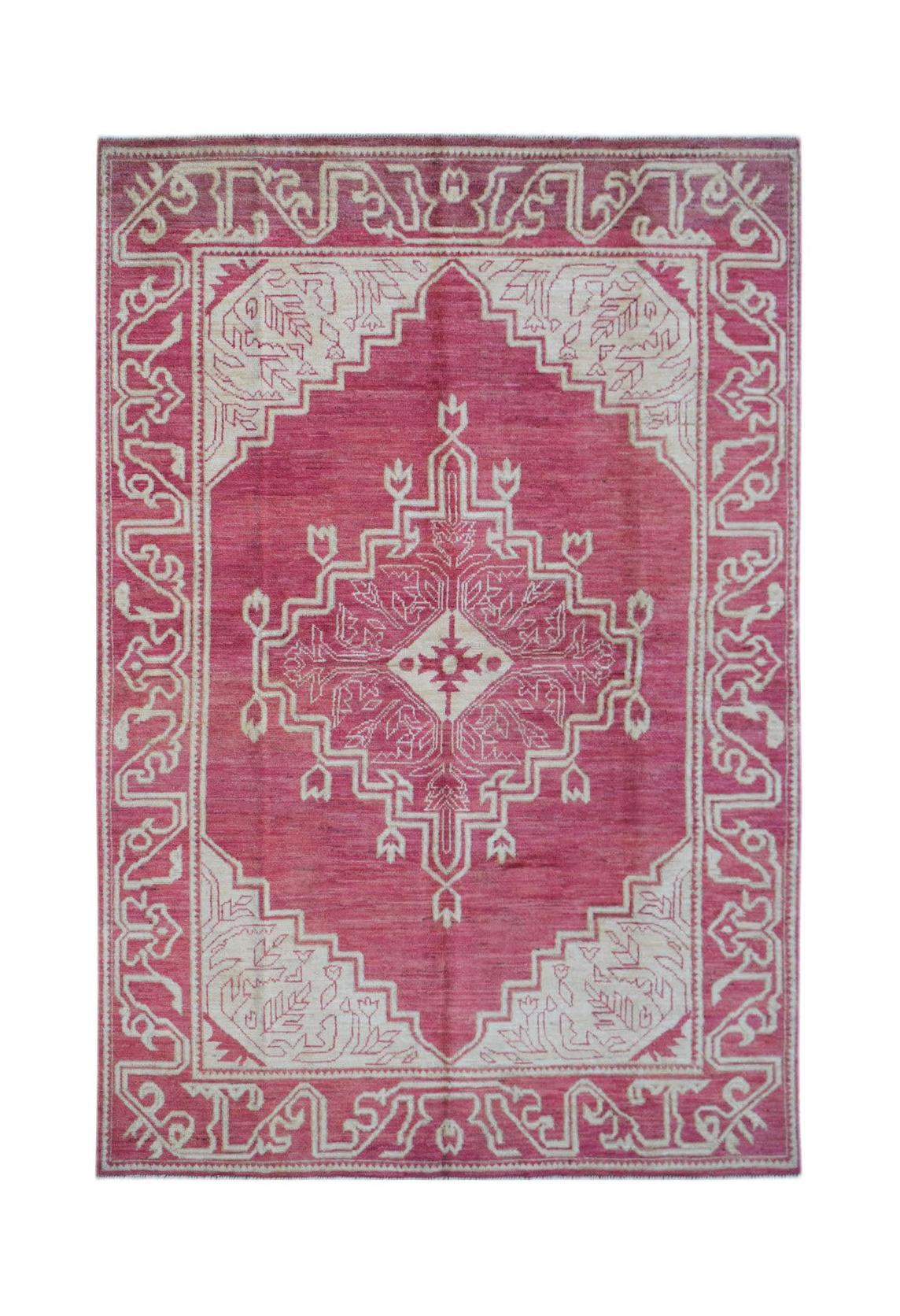A handmade wool rug from Afghanistan featuring a pink field with a white geometric medallion.