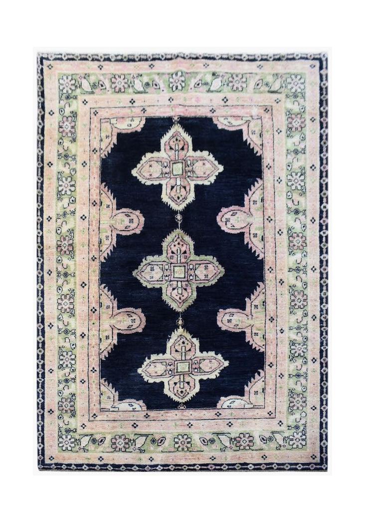 A handmade wool rug featuring a dark blue field with three pink and green floral medallions.