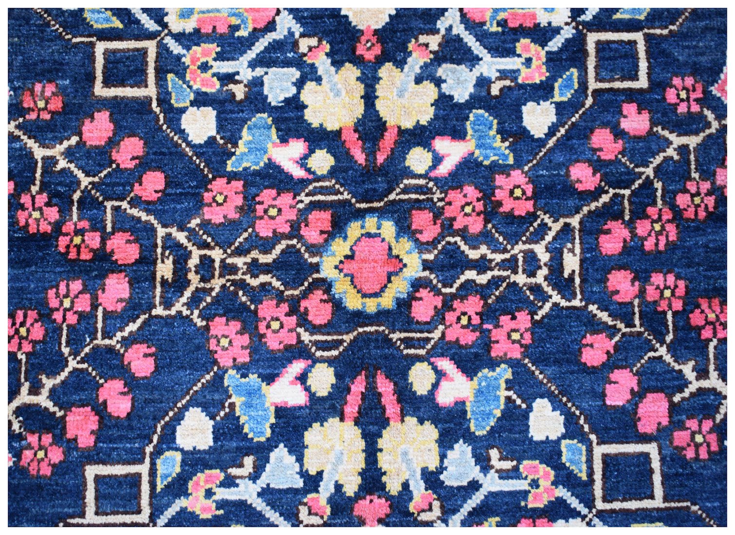 A handmade Afghan wool rug featuring a symmetrical floral pattern in pink, blue, and yellow.