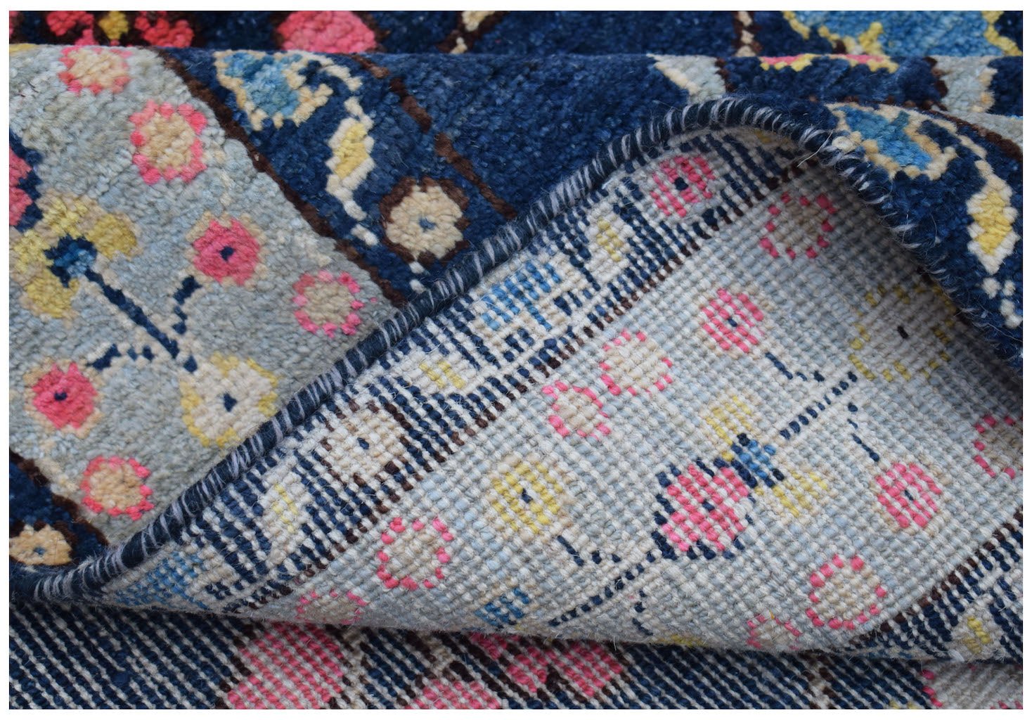 A close-up view of a handmade Afghan wool rug showing its blue and floral patterned pile.