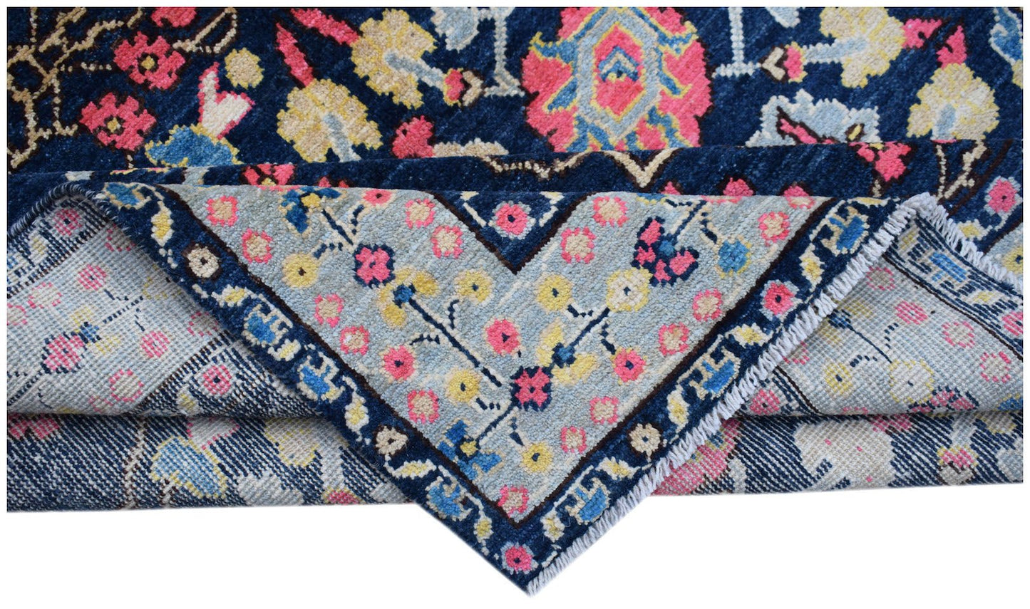 A handmade Afghan wool rug featuring a dark blue field with pink and yellow floral patterns.