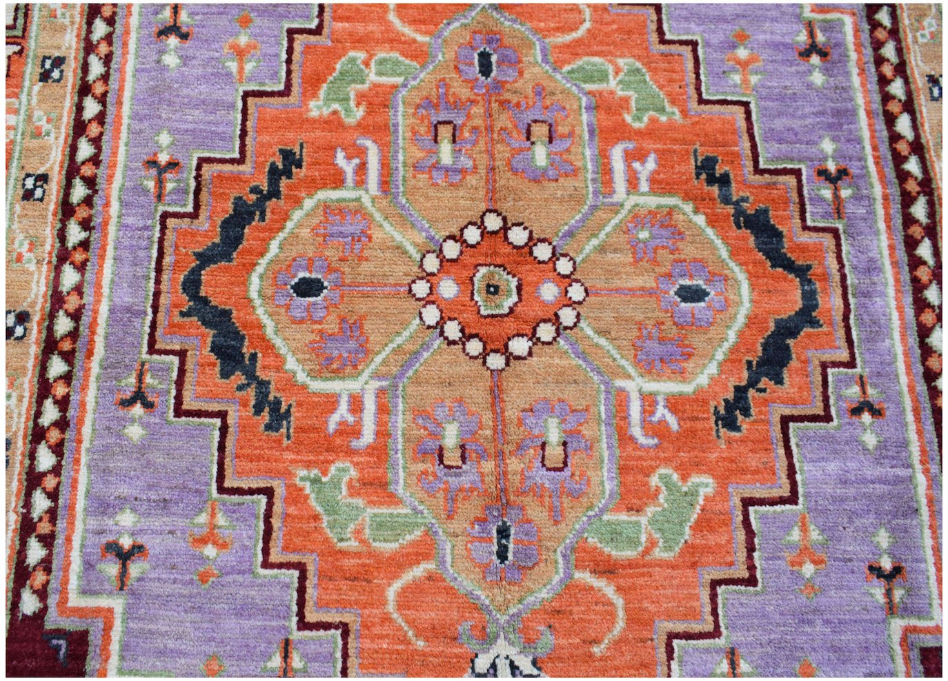 A handmade Afghan wool rug featuring a geometric orange medallion on a purple field.