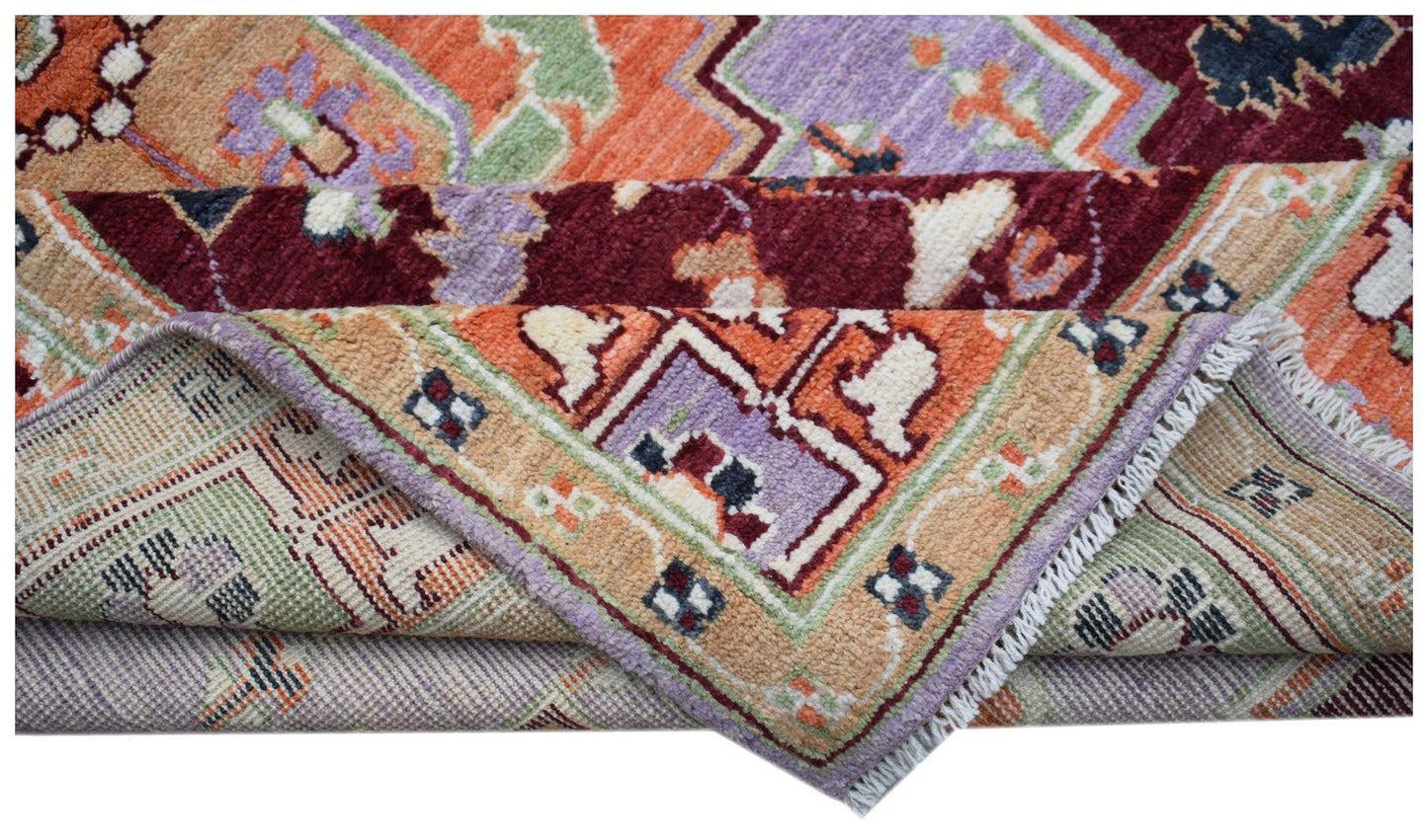 A folded Afghan Pashm rug featuring a vibrant geometric pattern in orange, purple, and red wool.